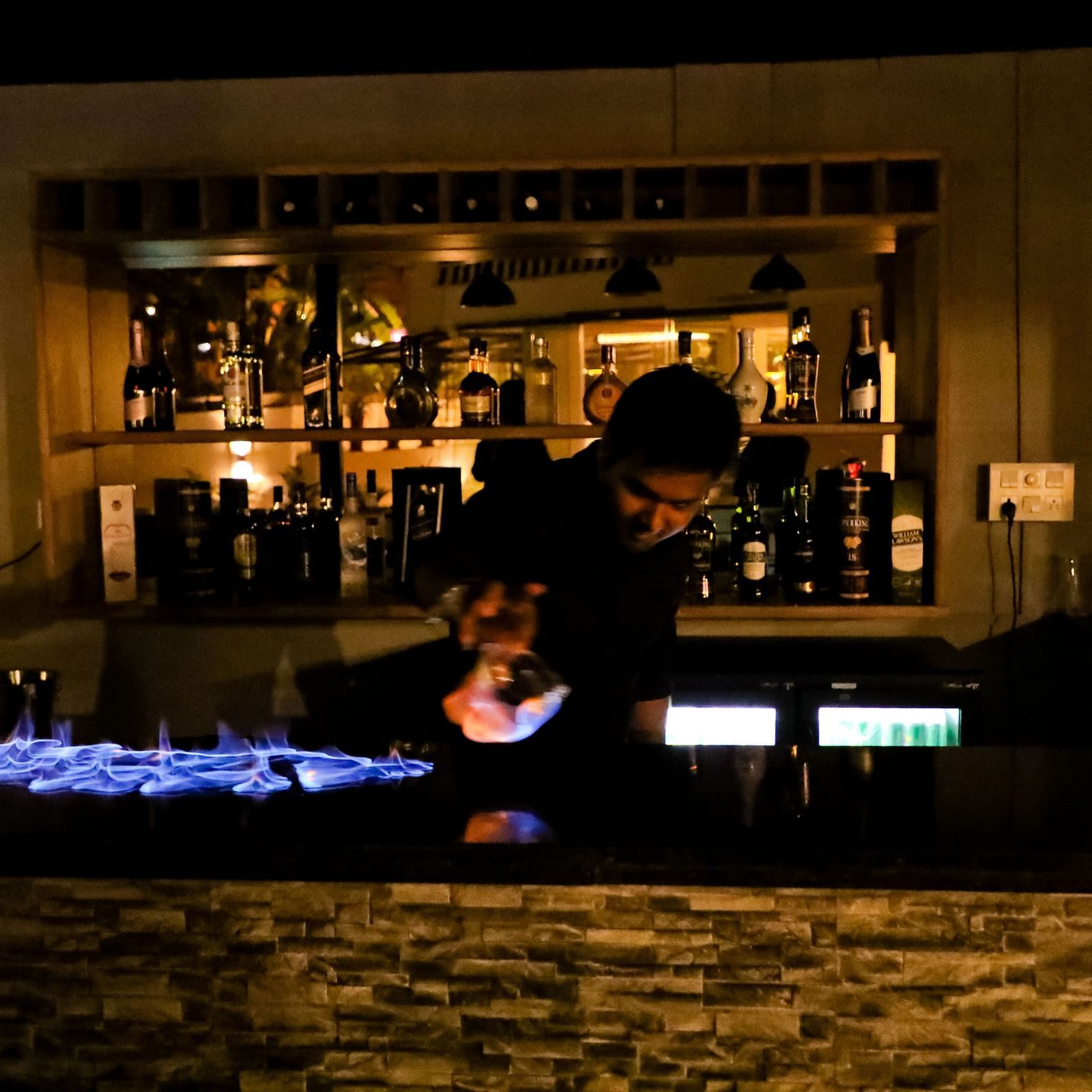 Image of a man behind a counter table with drinks on the shelf behind him at Calux Grand Baga.